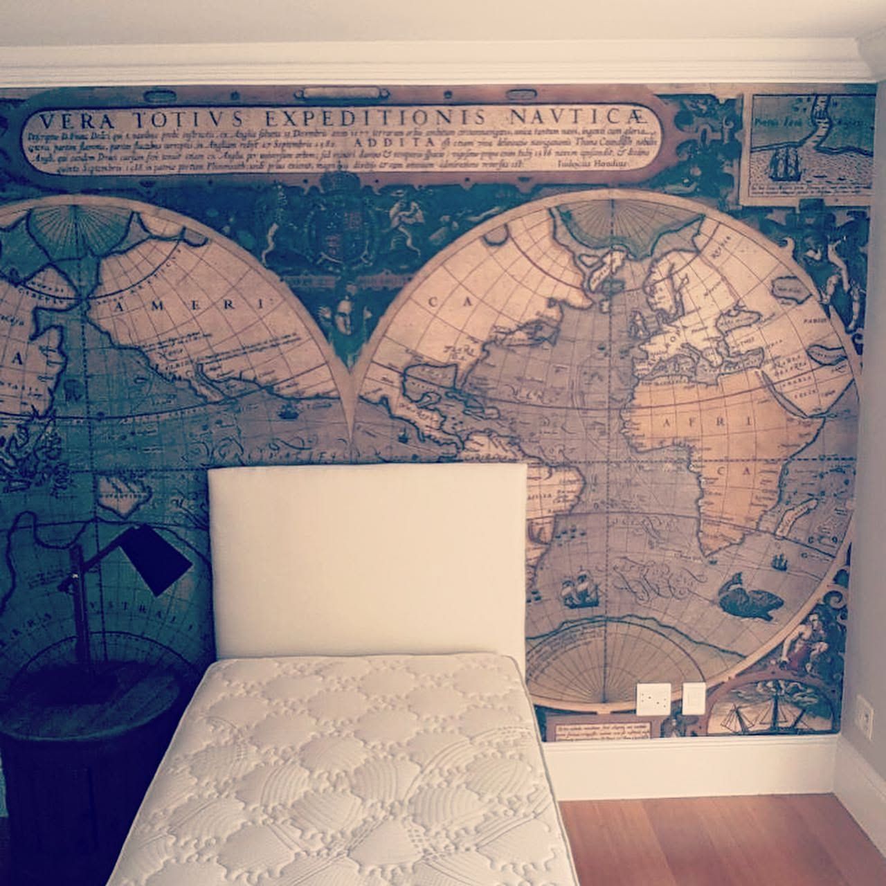 Antique world map mural behind a single bed