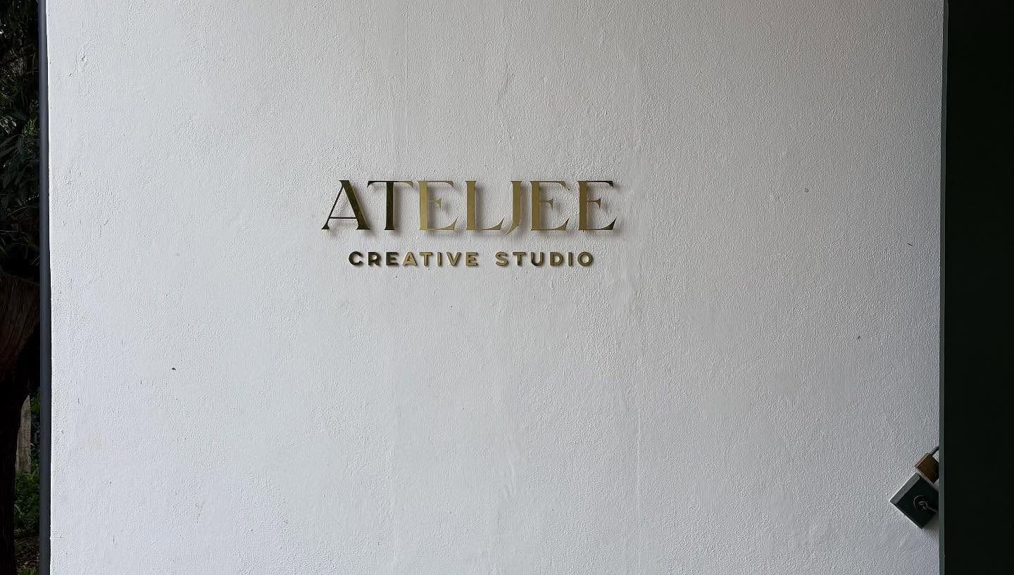 Atelier Creative Studio lettering in brushed brass on a white wall