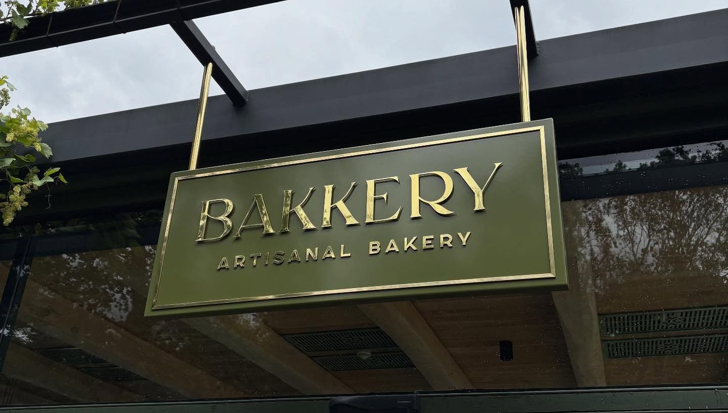 Hanging green and gold Bakkery Artisanal Bakery sign under a steel canopy