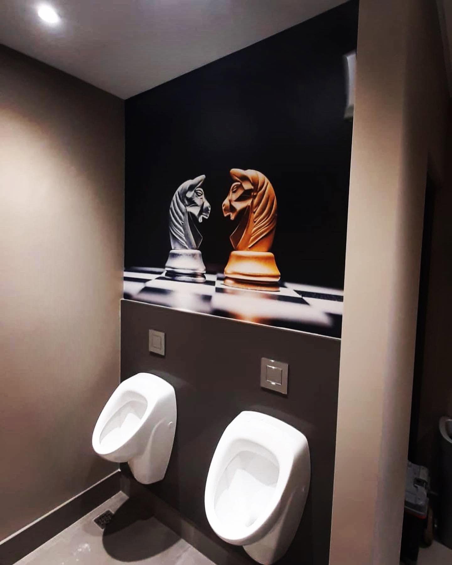 Black and white chess knights mural above urinals in a dark washroom