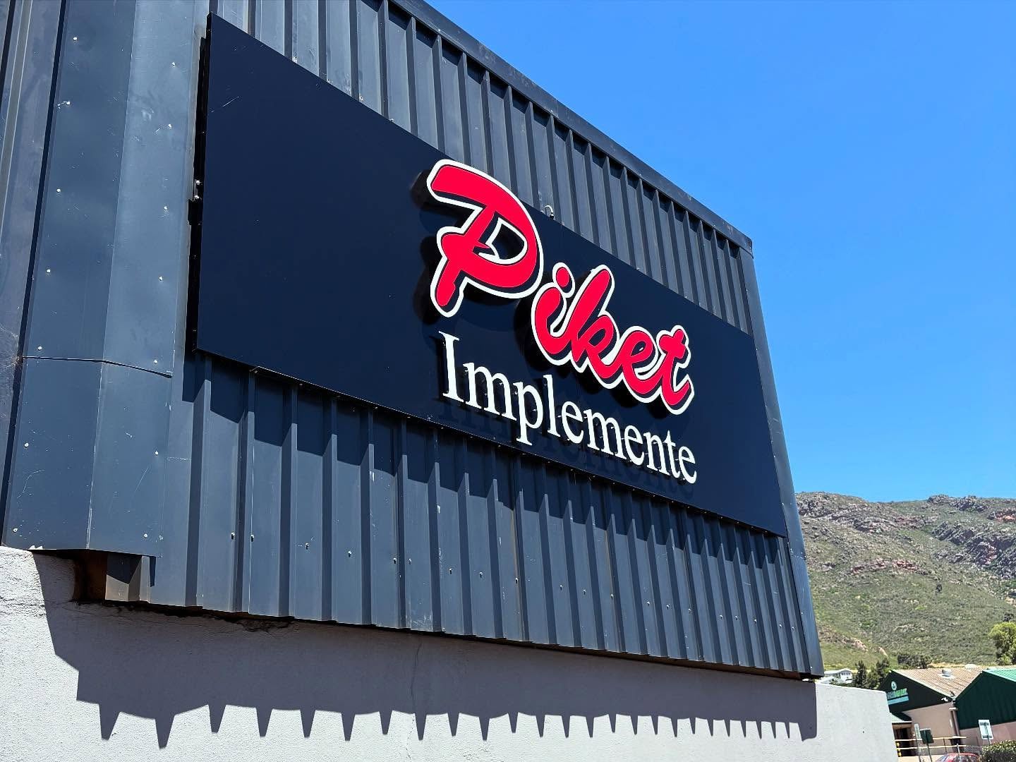 Navy Piket Implemente sign panel on dark metal cladding with mountains behind