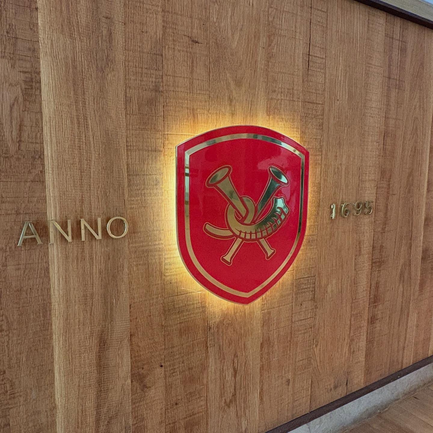 Halo-lit La Motte crest and brushed metal lettering on an oak-clad wall