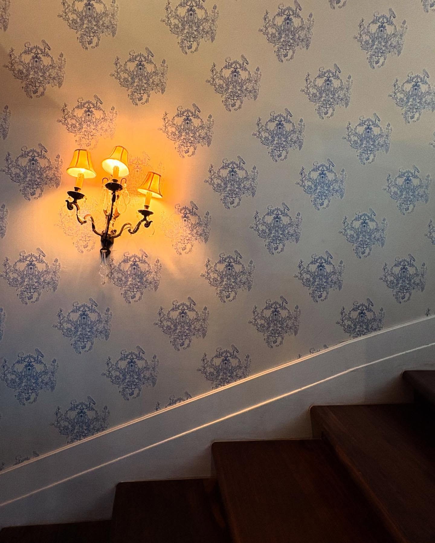 Brass sconce glowing against blue damask wallpaper on a stairwell
