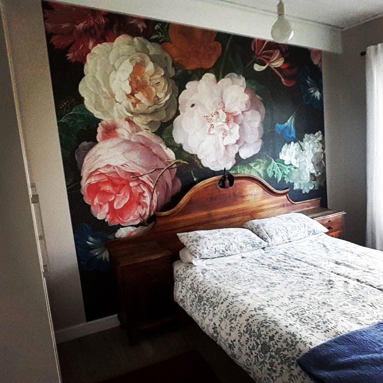 Dark floral mural of oversized peonies behind a wooden bed
