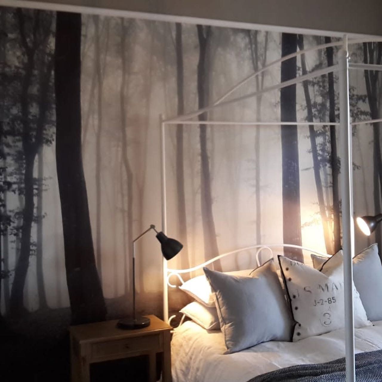 Misty forest mural behind a white four-poster bed