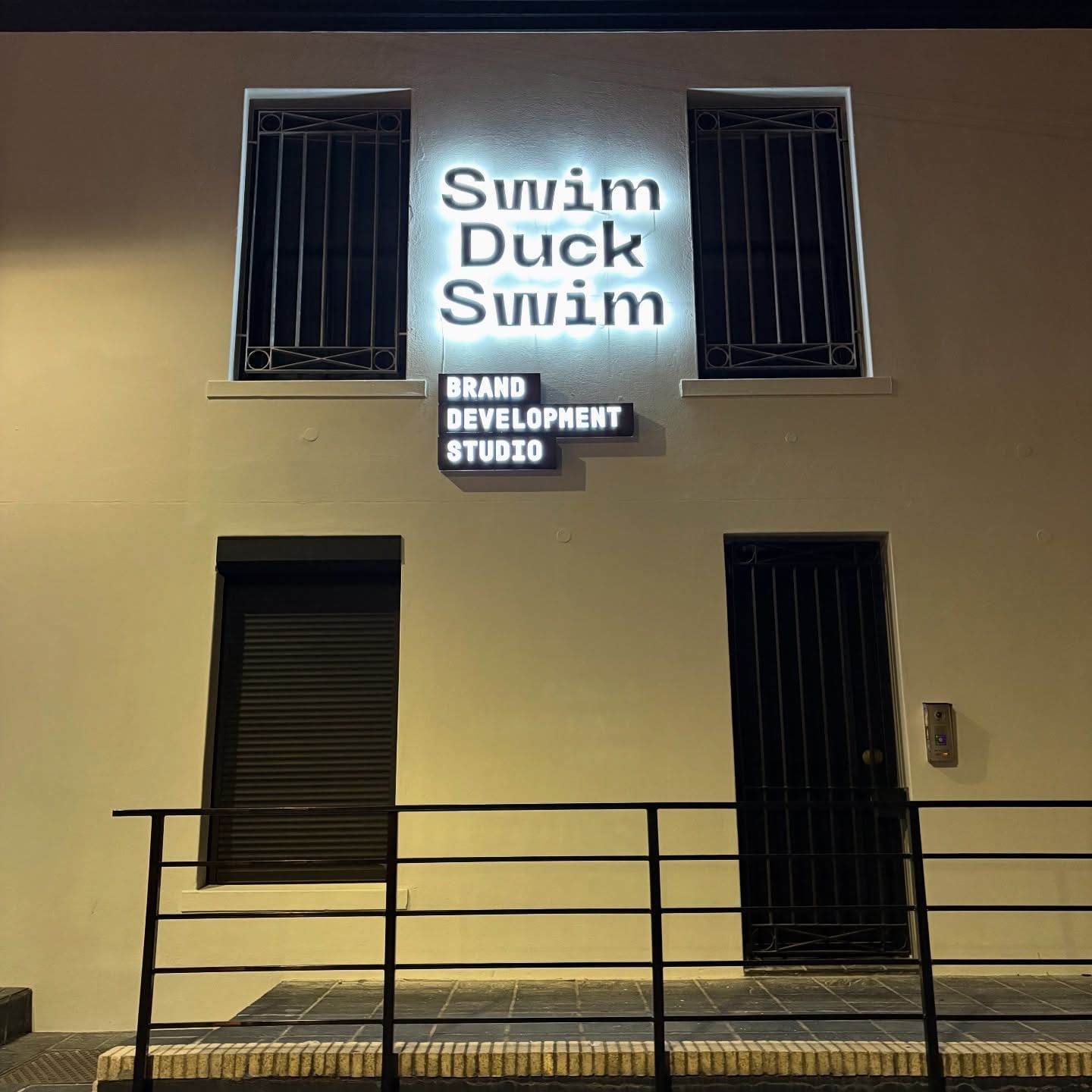 Swim Duck Swim lettering lit up on the upper wall at night, above a projecting sign