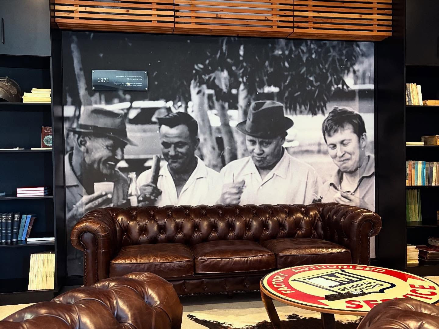 Black and white photographic mural of three men behind a leather chesterfield