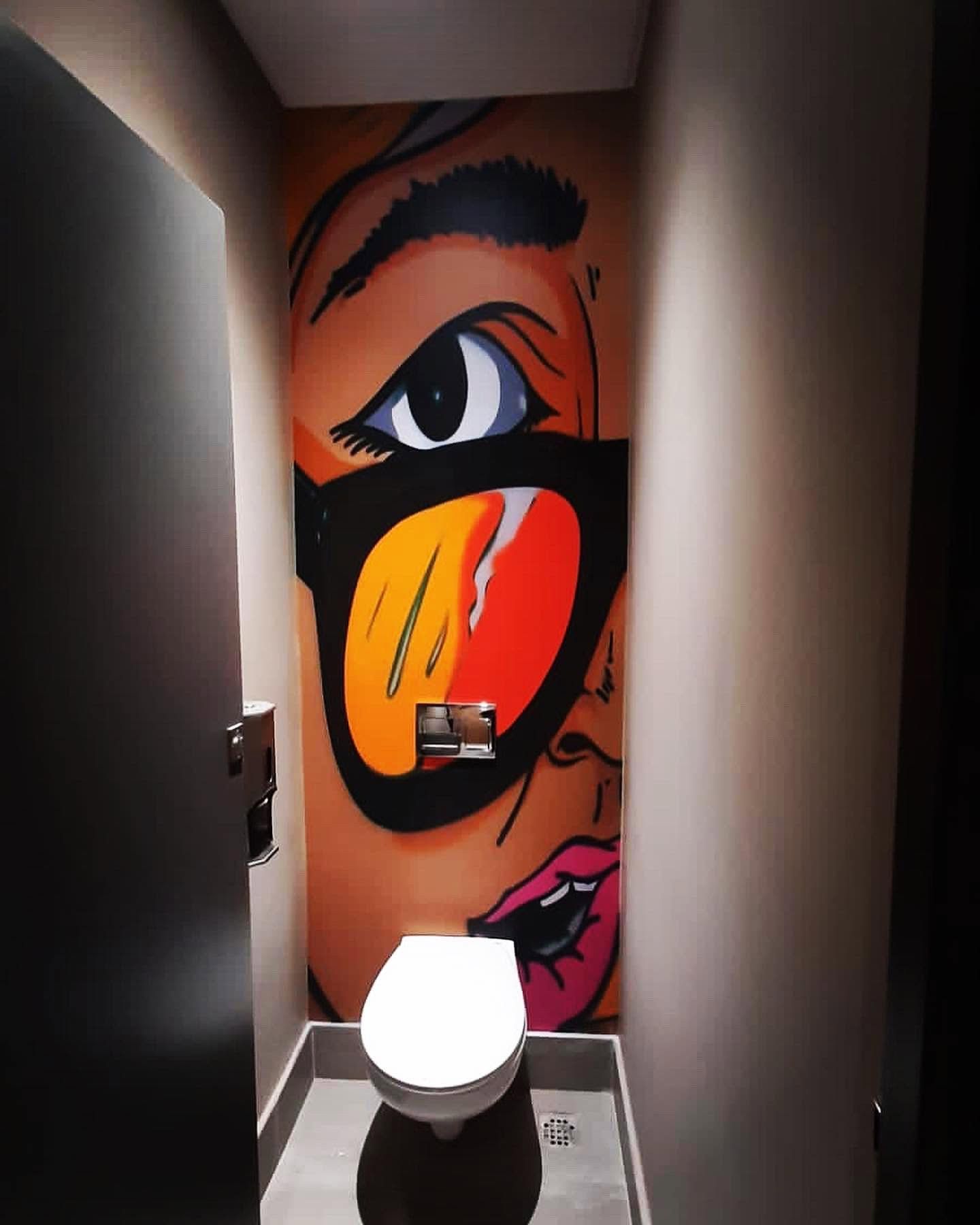 Pop art mural of a face with orange sunglasses behind a toilet