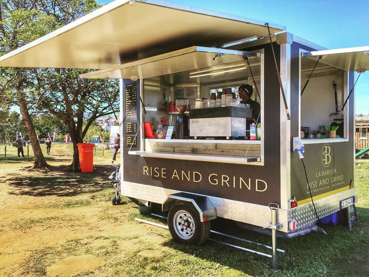 Rise and Grind coffee trailer with branded awning panels at an outdoor market