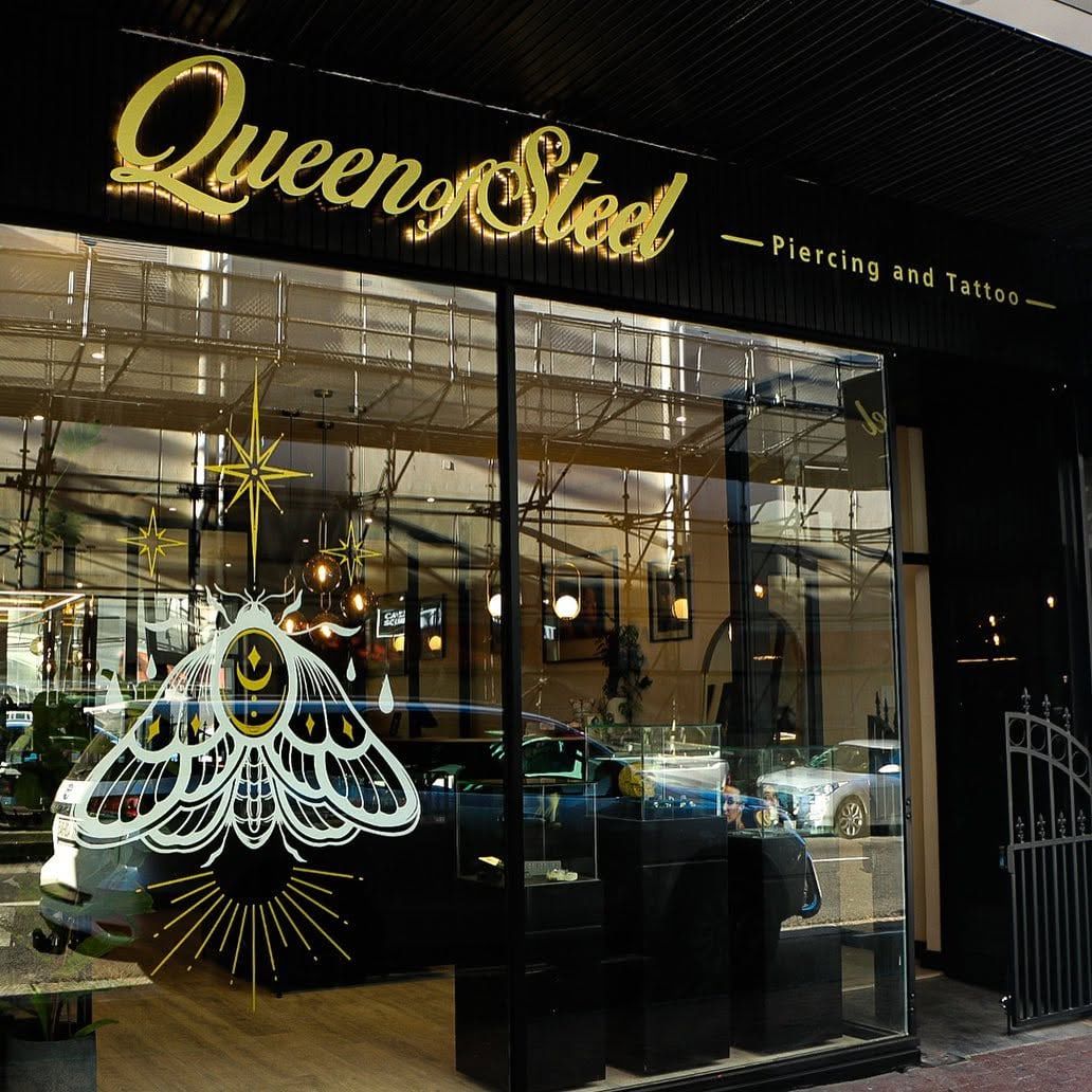Queen of Steel piercing and tattoo shopfront with gold script lettering and a moth on the glass
