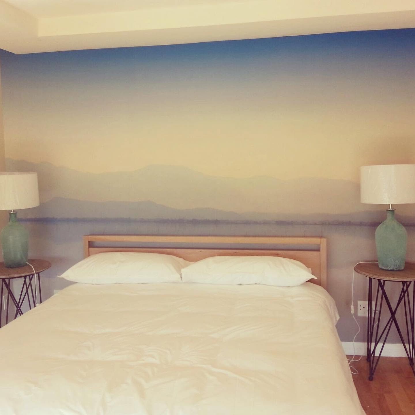 Soft sky and mountain mural behind a bed