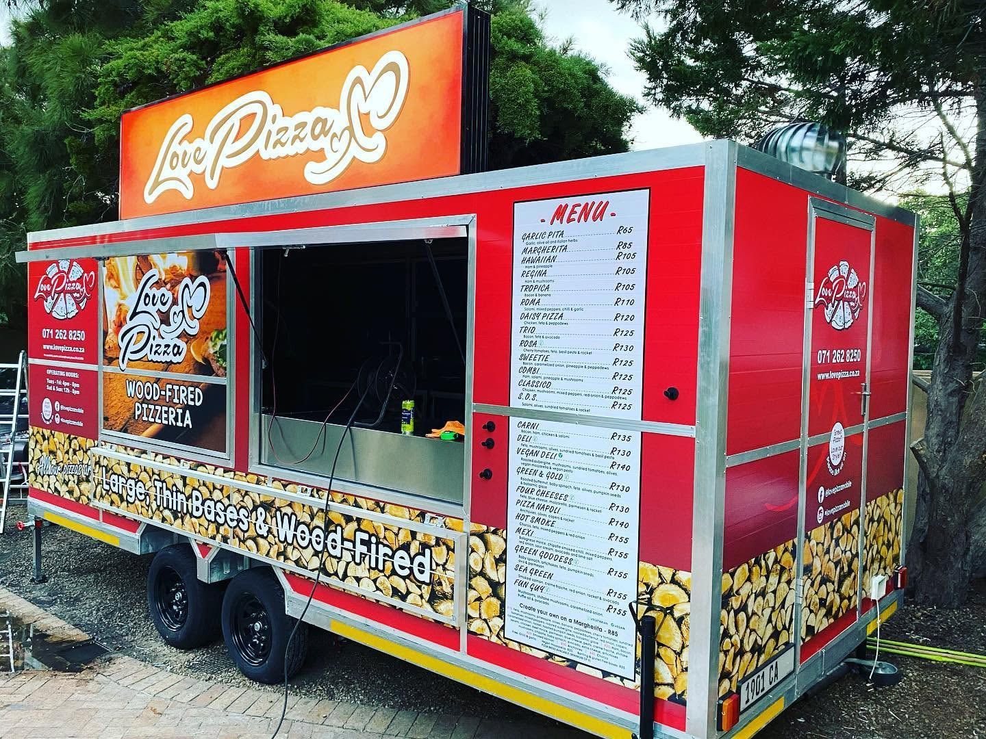 Side of the Love Pizza trailer with menu boards and a log-pile print